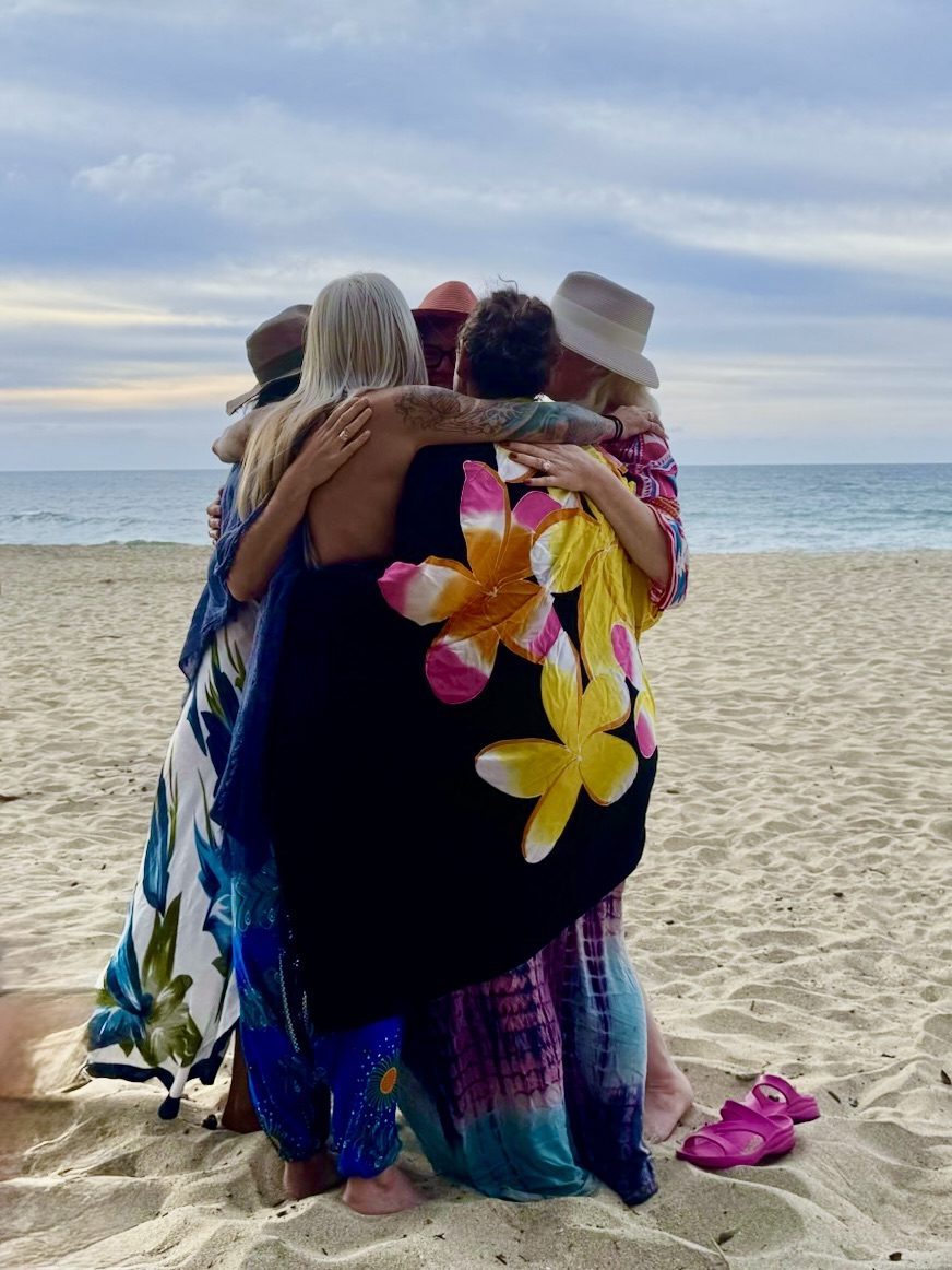A group of women holding each other on the beach at dusk